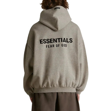 Person wearing a beige hoodie with 'ESSENTIALS FEAR OF GOD' text on the back against a white background