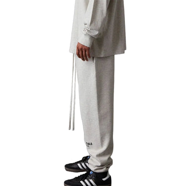 Person wearing gray sweatpants with a brand logo, standing on a white background